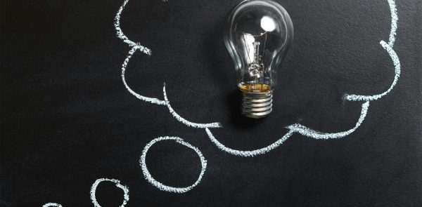 Light bulb laying on chalkboard with drawn thought bubble, symbolizing creative ideas.