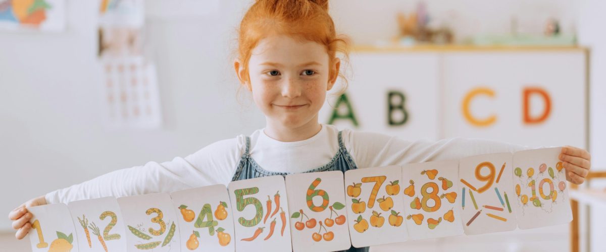 Young girl showcasing number cards in a vibrant classroom setting.